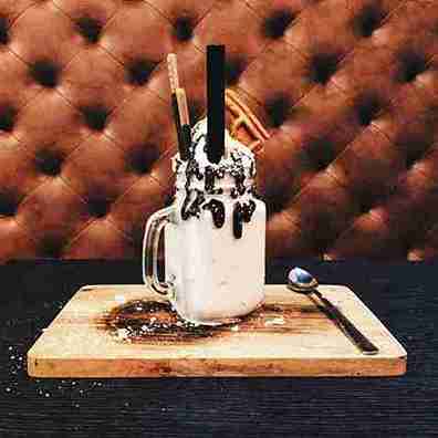Delicious Oreo milkshake topped with whipped cream, chocolate drizzle, and wafers on a wooden board