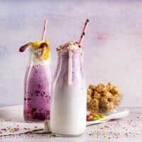 “Refreshing berry and vanilla milkshakes in glass bottles topped with whipped cream, sprinkles, and gummy candies — colorful dessert shakes for summer treats.”