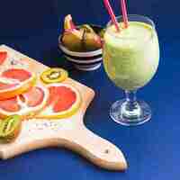 “Glass of fresh kiwi smoothie served with sliced grapefruit and kiwi on a wooden board — healthy breakfast smoothie rich in vitamin C and antioxidants.”