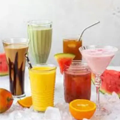 A variety of colorful refreshing summer drinks arranged together, including mango smoothie, chocolate shake, green detox juice, iced tea, and pink watermelon smoothie served with fresh fruit slices and ice cubes on a white background."