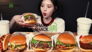 The Korean-Style Menu is back at Shake Shack as a young woman reacts to multiple burgers with juicy beef patties and fresh toppings.