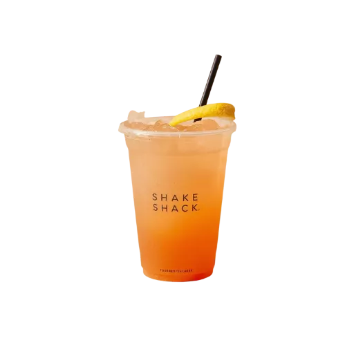 A vibrant orange-tinted Shake Shack seasonal lemonade served in a clear branded cup with crushed ice, a fresh lemon slice, and a black straw, isolated on a dark background.